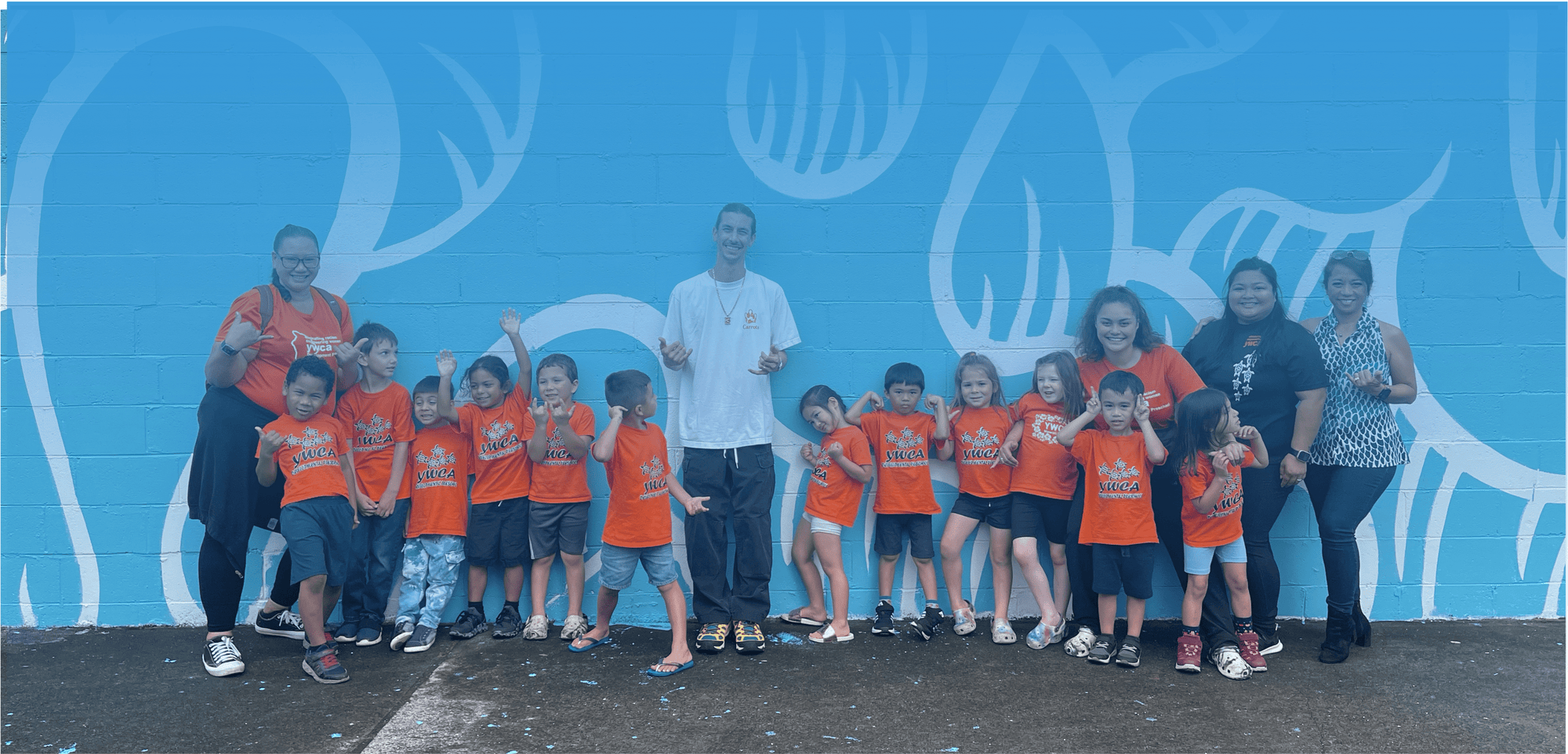 Group of children and adults in orange shirts in front of blue mural wall
