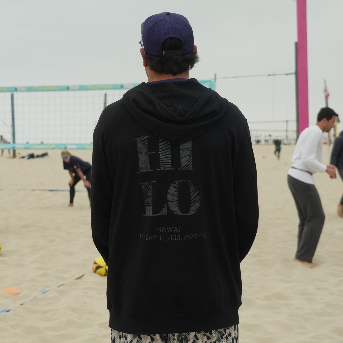 Man in hoodie watching beach volleyball game
