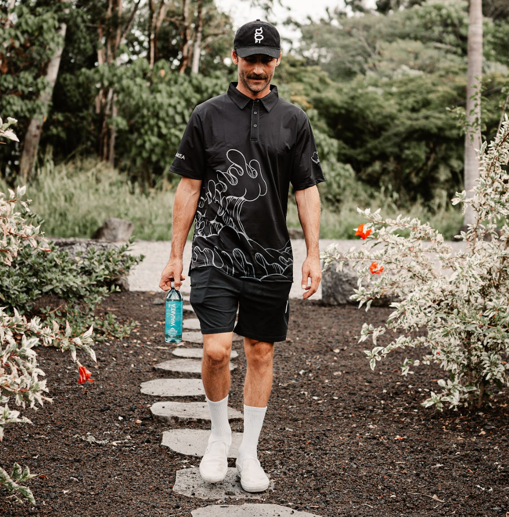 Man walking in garden holding water bottle wearing black shirt and cap