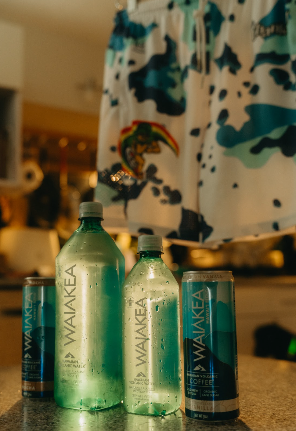 Waiakea Hawaiian volcanic water bottles and cans with colorful shorts hanging above.