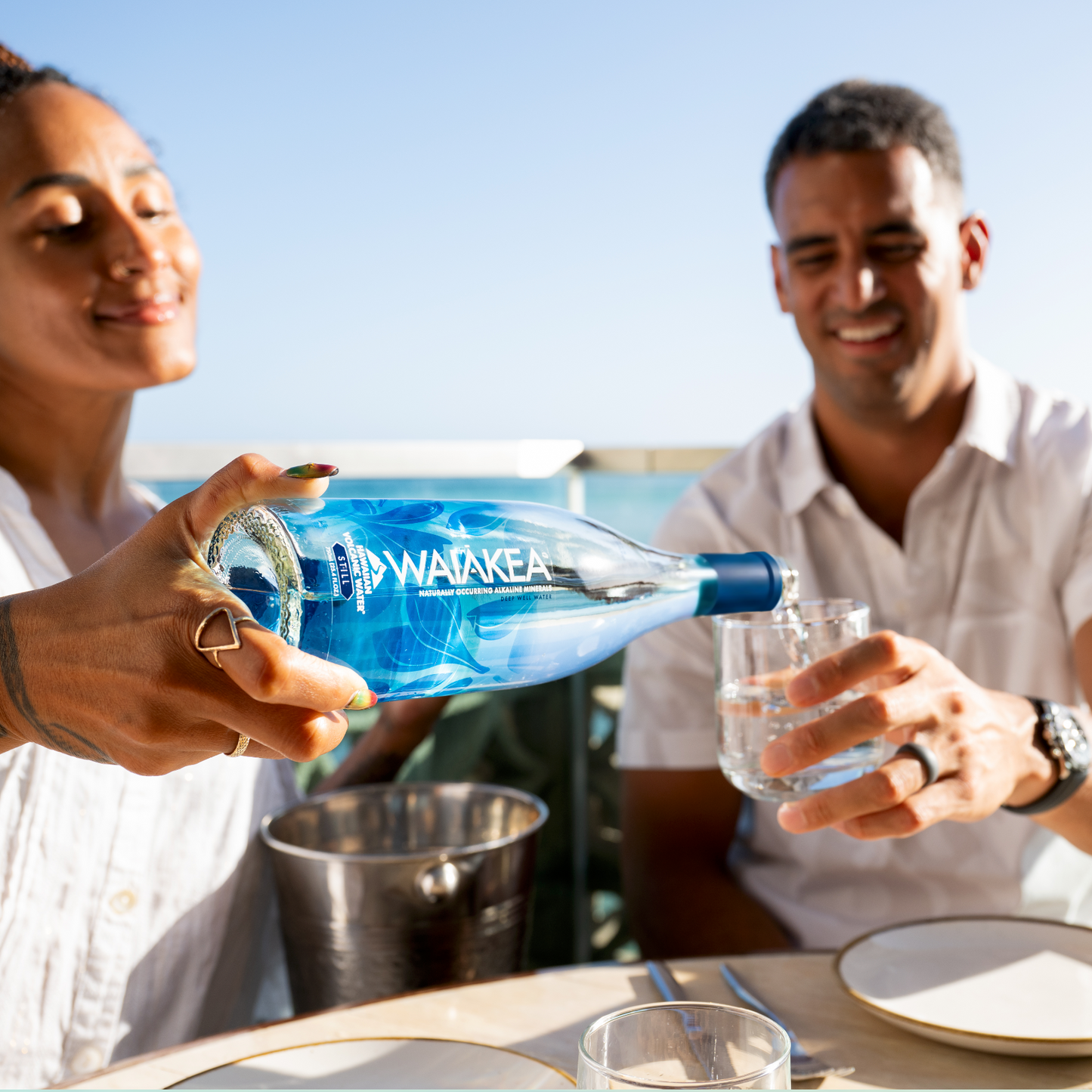Two people at a table with a Waiākea water bottle and glasses.