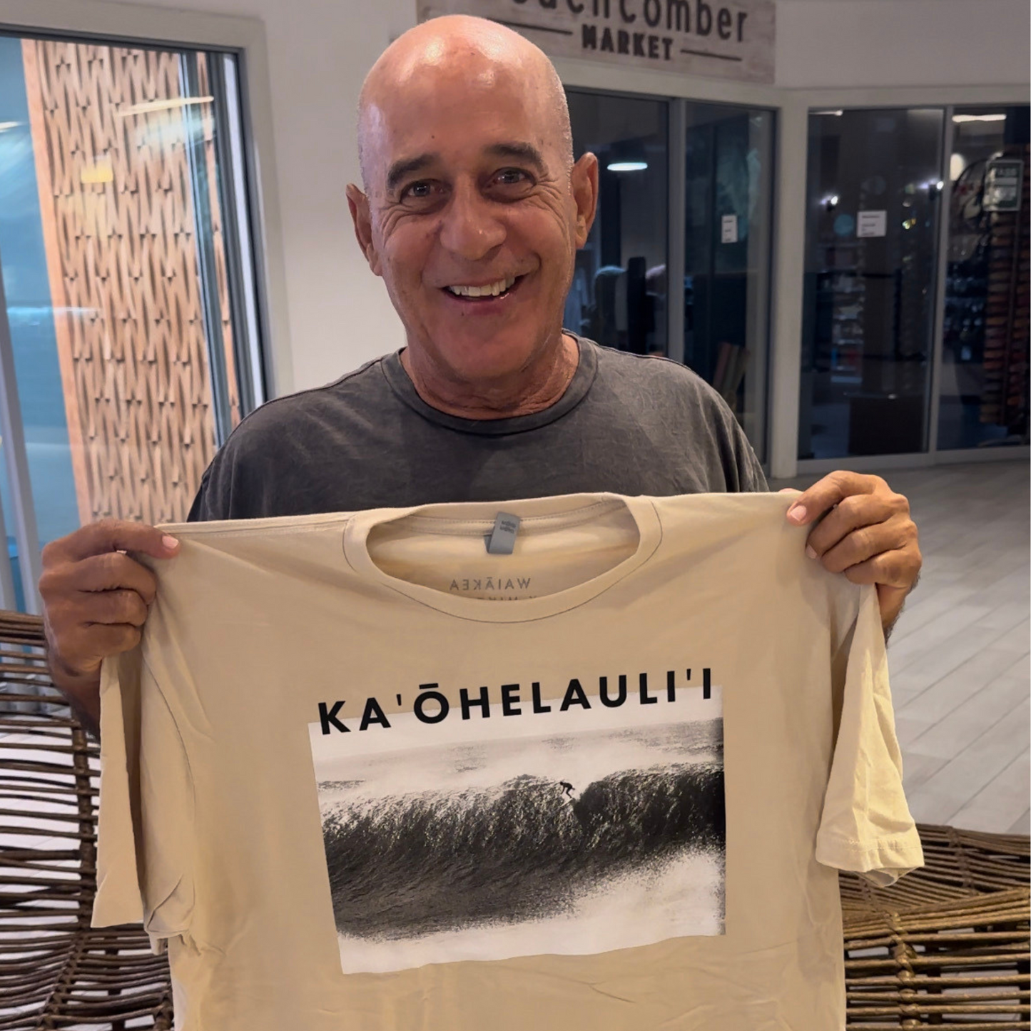 Man holding Ka'ohelauli'i t-shirt with wave design.