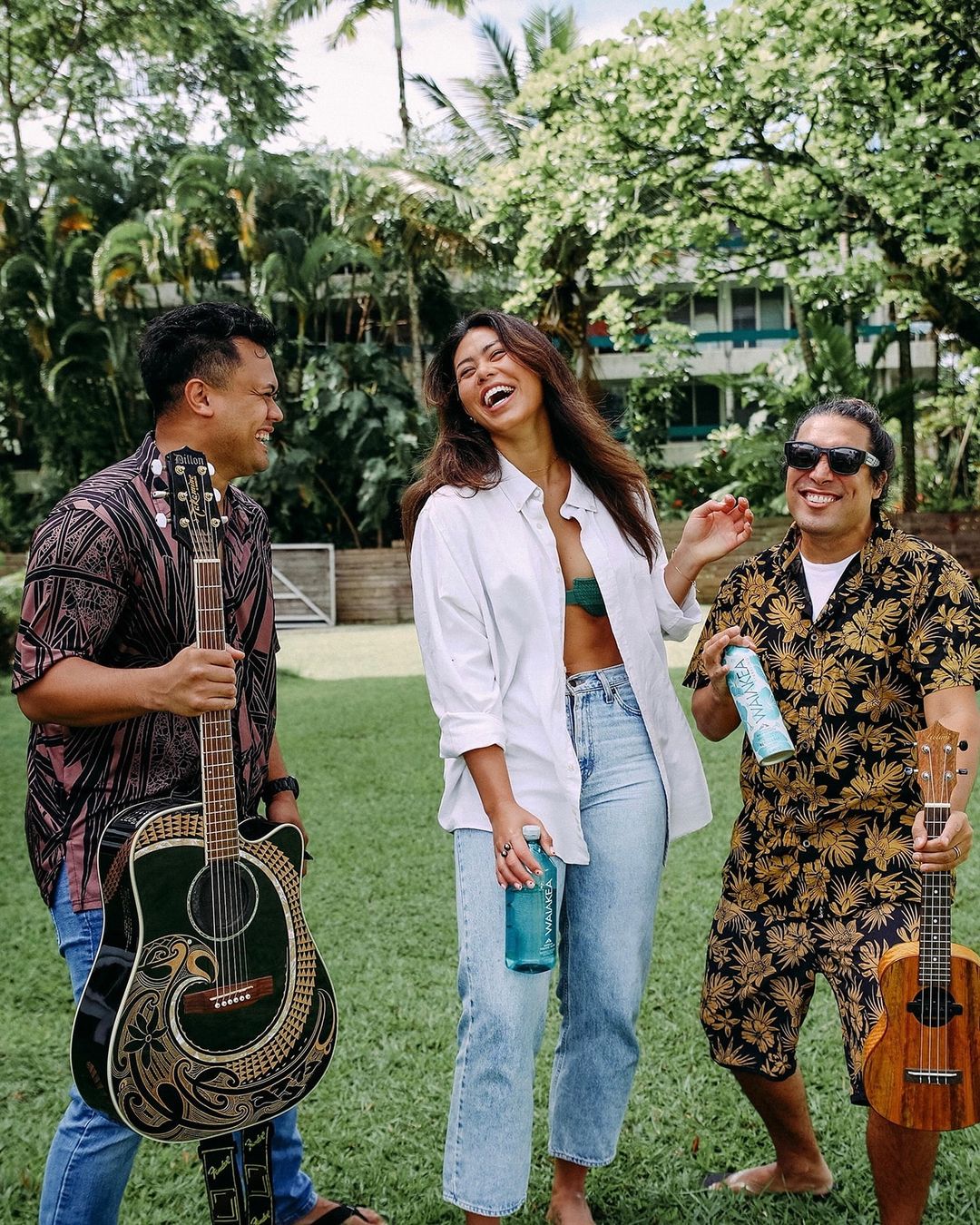 People laughing with guitars in a tropical setting.
