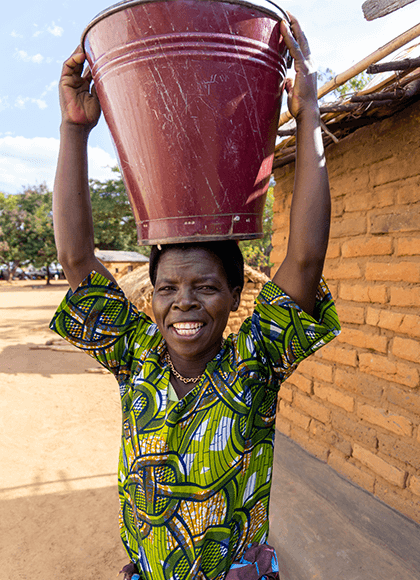 Person carrying bucket on head in rural area with colorful shirt