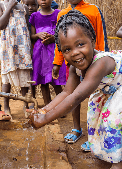 Child smiling washing hands at outdoor water tap.