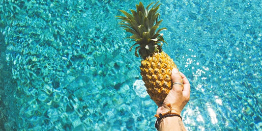 Person holding a pineapple above a pool