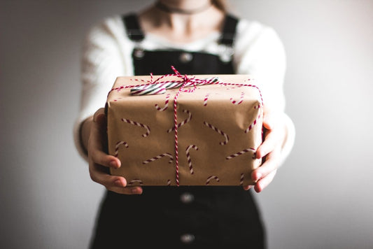 A person giving a gift wrapped in candy cane newspaper