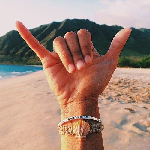 Hand throwing a shaka on the beach in front of a mountain