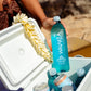 Person holding a Waiakea bottle over an open cooler with other drinks inside.