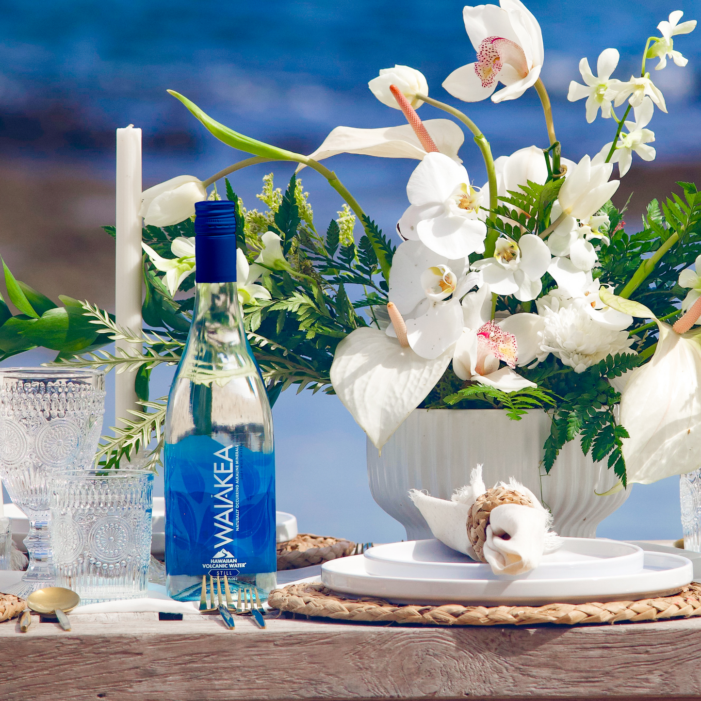 Waiākea bottle on a table with flowers and seashells against a blue ocean background