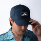 man wearing a blue performance hat with a rubber patch with the Waiākea logo on it 