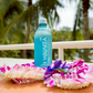 Waiakea bottle on a table with tropical flowers and blurred palm trees in the background