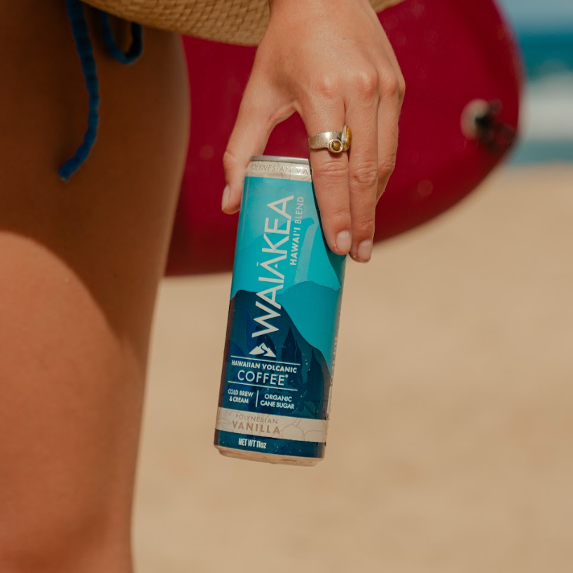Person holding a Waiakea coffee can on a beach