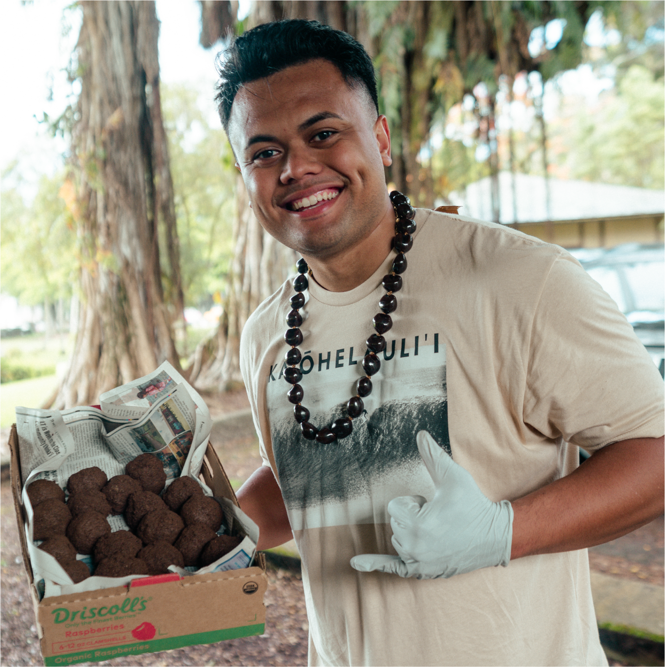 Man holding box of food wearing necklace outdoors.