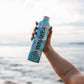 hand holding Waiakea water bottle beach background